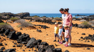 Une mère, un père et deux enfants observent prudemment un petit lézard dans un paysage volcanique de Lanzarote.
